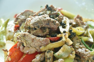 Baharatlı kızarmış devekuşu eti, soğan ve tabakta karabiber.