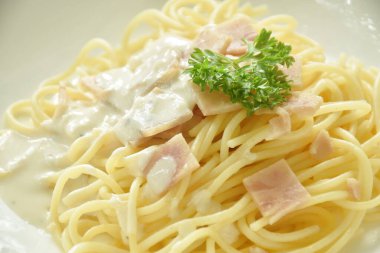 Buharda pişirilmiş spagetti beyaz kabonara krema sosu dilimlenmiş domuz eti tabakta. 