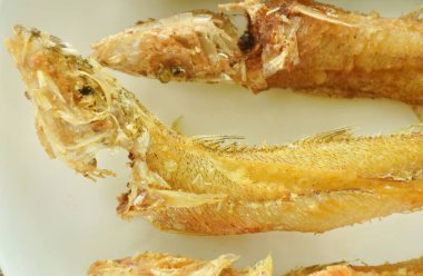 Kızarmış kum mezgit balığı tabağa dizilmiş baharatlı acı biber sosunu fincana bandırıyor.