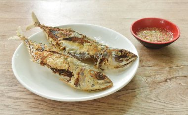 Kızarmış taze uskumru balığı tabağa dizilmiş baharatlı acı biber sosunu fincana bandırıyor.  