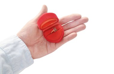 Kırmızı kadife yüzük kutusundaki mor mücevher. Erkek eli şeklinde. Beyaz arka planda evlenmek istiyor.