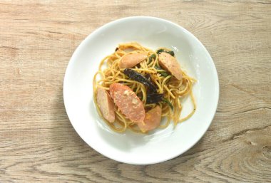 Baharatlı kızarmış spagetti dilimlenmiş domuz sosisi kuru biber ve tabakta fesleğen yaprağı.