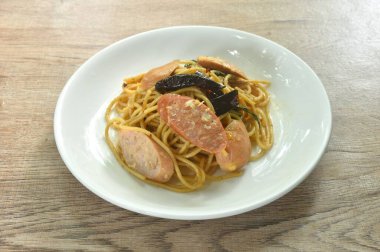 Baharatlı kızarmış spagetti dilimlenmiş domuz sosisi kuru biber ve tabakta fesleğen yaprağı.