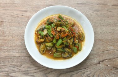 Baharatlı kızarmış midye dilimlenmiş uzun fasulye ve tabakta fesleğen yaprağı. 