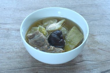 Haşlanmış lahana turşusu ve domuz kemikli acı salatalık üstü siyah mantar kabın üzerinde berrak çorba. 