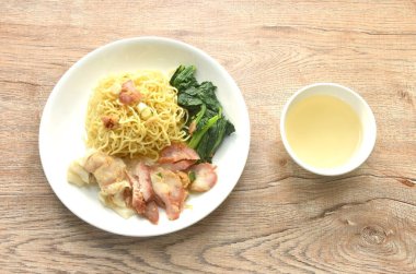 Kuru Çin yumurtası, sarı erişte, kırmızı ızgara domuz eti ve şeffaf çorba bardağıyla tabakta hamur tatlısı.