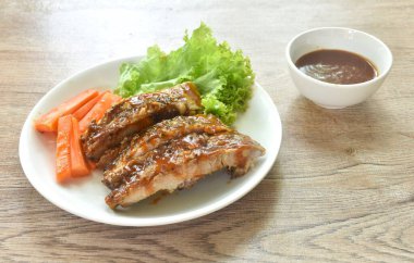 Izgara domuz kaburgası, havuç ve marul tabağa batırılmış barbekü sosu.