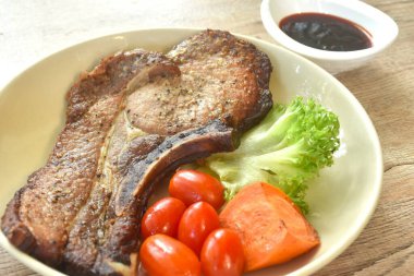 Izgara karabiberli domuz pirzolası biftek ve domatesli marul tabakta haşlanmış havuç bardağa batırılmış barbekü sosu.