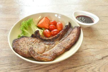 Izgara karabiberli domuz pirzolası biftek ve domatesli marul tabakta haşlanmış havuç bardağa batırılmış barbekü sosu.