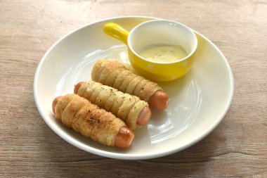 Kızarmış kızarmış roti ekmeği rulo halinde füme tavuk sosisi mayonez sosu tabakta.