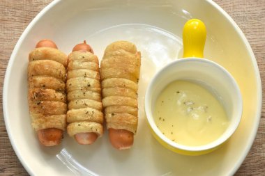 Kızarmış kızarmış roti ekmeği rulo halinde füme tavuk sosisi mayonez sosu tabakta.