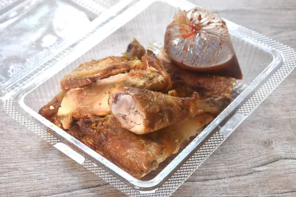 Kızarmış tavuk eti kanadı ve bacağı şeffaf plastik ambalajda baharatlı sosla bandırılmış.