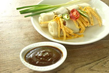 Un ambalajlı Çin böreği ve fasulye filizi soslu domuz eti. Tabakta kırmızı sos var.   