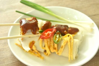 Un ambalajlı Çin böreği ve fasulye filizi soslu domuz eti. Tabakta kırmızı sos var.   