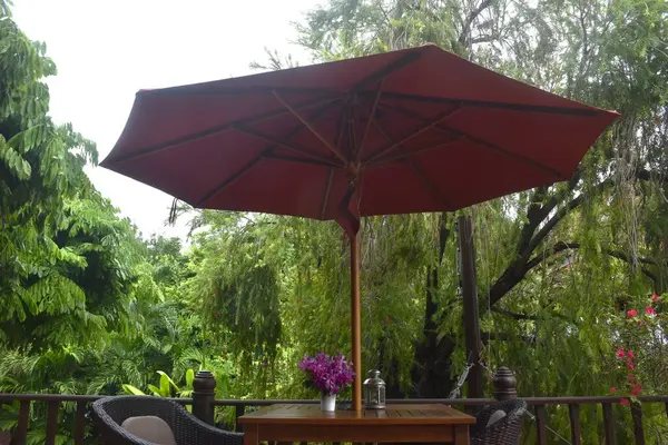 Çiçek saksısıyla süslenmiş mavi orkide ve ahşap masada fener ve terasta uzun kırmızı şemsiye sapı var.