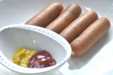 Tütsülenmiş İtalyan sosisi tabaklara yerleştirilmiş ketçap ve hardal sosu.