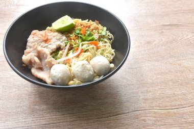 dry Chinese egg yellow noodles topping boiled chop pork with pork ball dressing cayenne pepper couple shrimp on bowl