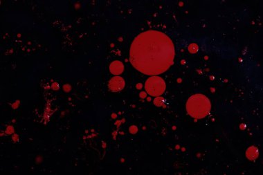 Bright red paint splashes on a thinner solution forming an abstract pattern. Selective focus on black background.