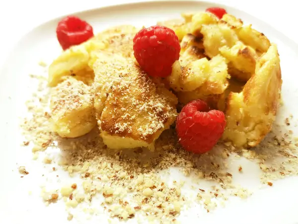 Kaiserschmarrn mit frischen Himbeeren ist eine kstliche sterreichische Sspeise. Der luftige Pfannkuchen wird mit Zucker bestreut und mit Himbeeren serviert, ein Genuss fr alle Naschkatzen!