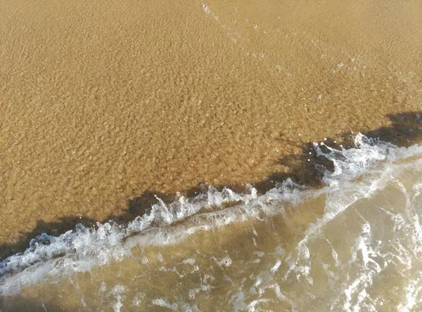 Das wunderschoene tuerkis farbige Meerwasser ueberspuehlt den wunderschoenen sauberen Sandstrand. Man kann die Wellen Erkennen und erkenlich das Salz im Wasser.