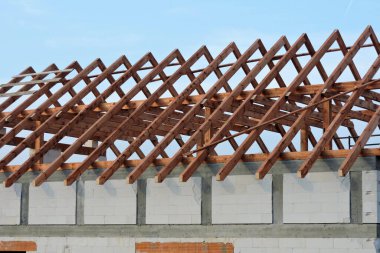 İnşaat halindeki bir evde ahşap çatı kirişi, otomatik klavsenli beton bloklardan yapılmış duvarlar, güçlendirilmiş beton kiriş ve arka planda güçlendirilmiş beton sütunlar, mavi gökyüzü.