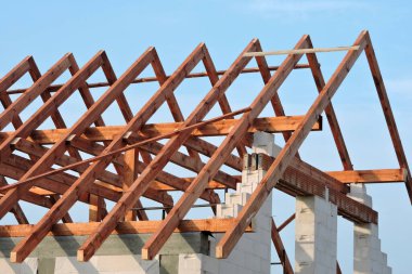 Kereste çatı kirişleri, otomatik klavuzlu beton bloklardan yapılmış duvarlar, güçlendirilmiş beton kiriş ve kolonlar, kaba bir pencere açılışı, güçlendirilmiş tuğla kiremitler, arka planda mavi gökyüzü.
