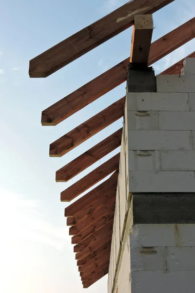 Wooden rafters and a wall plate, walls made of autoclaved aerated concrete blocks, a reinforced concrete beam, blue sky in the background