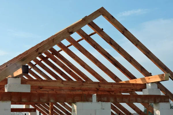 A timber roof truss in a house under construction, walls made of autoclaved aerated concrete blocks, rough window openings, a reinforced brick lintel, blue sky in the background