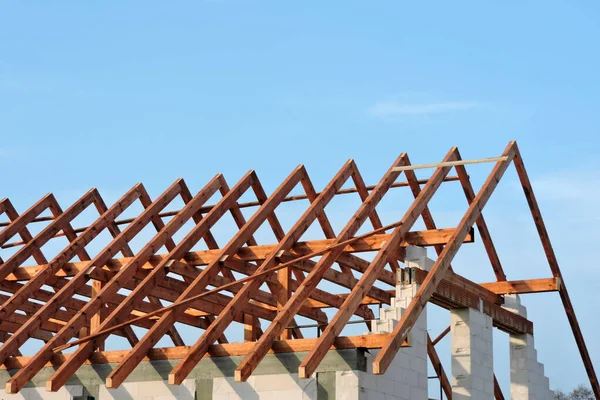 A timber roof truss in a house under construction, walls made of concrete blocks, rough window openings, a reinforced concrete beam and reinforced concrete columns, blue sky in the background