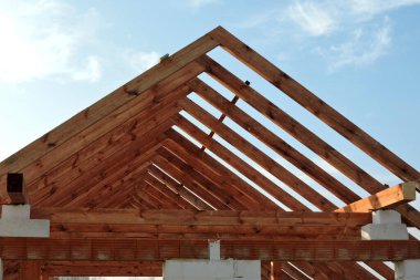 İnşaat halindeki bir evde ahşap çatı kirişi, otomatik klavsenli beton bloklardan yapılmış duvarlar, kaba pencere aralıkları, güçlendirilmiş tuğla kaplama iskelesi, arka planda mavi gökyüzü.