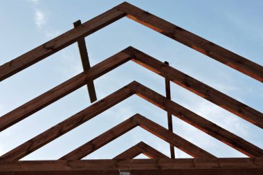 İnşaat halindeki bir evin ahşap çatı kirişi, arka planda mavi gökyüzü.