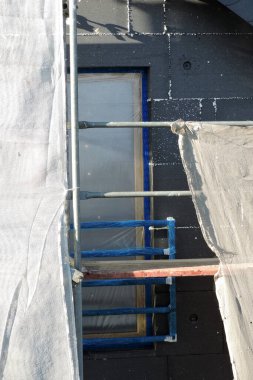 Isı yalıtımı için EPS grafit polistiren tahtalarla kaplı bir ev duvarı koruyucu bir film, iskele ve güneşli bir gün ile kaplı bir pencere.