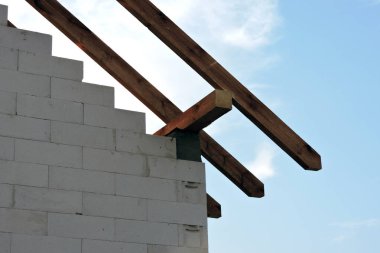 Wooden rafters and a wall plate, walls made of autoclaved aerated concrete blocks, blue sky in the background clipart