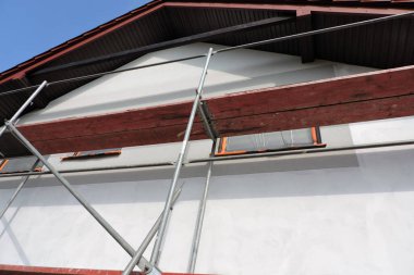 Dış duvarlar, pencereler ve pencere perdeleri koruyucu bir filmle kaplanmadan önce asal bir şekilde kaplanmış bir duvarın yanındaki iskele.