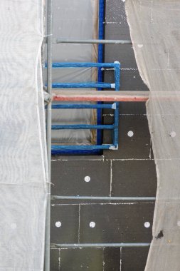 Termal yalıtım için EPS grafit polistiren tahtalarla kaplı bir ev duvarı, bir iskele iskelesi ve bina güvenlik iskelesi, koruyucu bir filmle kaplı bir pencere, beyaz plastik çapalar.