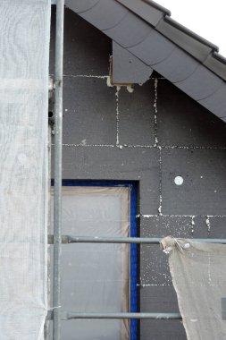 Termal yalıtım için EPS grafit polistiren panolarla kaplı bir ev duvarı koruyucu bir filmle kaplı bir pencere, bir iskele...