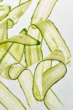 Beyaz Arkaplanda ince dilimlenmiş salatalık kurdeleleri. Taze, sağlıklı ve enerjik. Beyaz arka planda taze salatalık dilimleri, yakın plan.