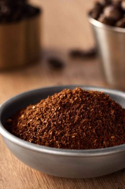 Bir kâsede Aromatik Ground Coffee Beans, demlenmeye hazır kahve tozu ve ahşap arka planda kahve çekirdeği.