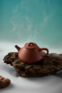 Rustik Kaya 'da Buharlı Yixing Çaydanlığı, Arkasında duman olan bir taşın üzerinde seramik çaydanlık