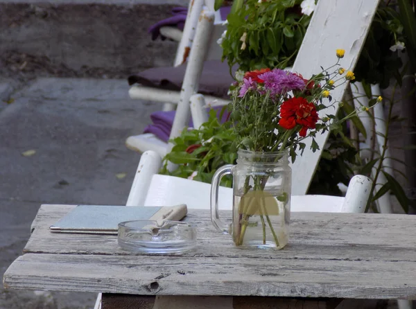 stock image White garden table with flowers in jar and chair with purple cushion on the terrace