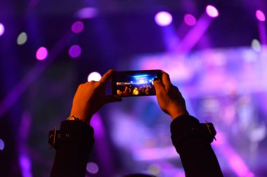 Konser sırasında sahneyi cep telefonuyla kaydeden kızın elleri.