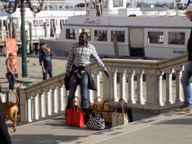 Venedik, İtalya - 8 Nisan 2018: Sokak satıcısı Venedik Limanı 'ndaki Riva degli Schiavoni köprüsünde çanta satıyor