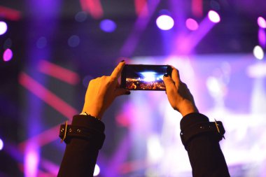 Konser sırasında sahneyi cep telefonuyla kaydeden kızın elleri.