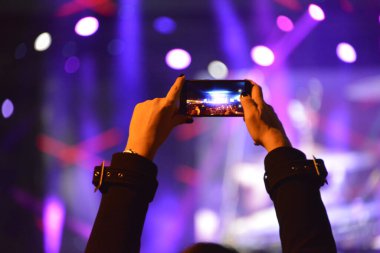 Konser sırasında sahneyi cep telefonuyla kaydeden kızın elleri.