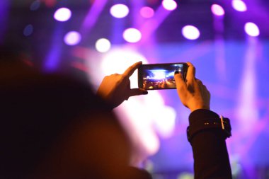 Konser sırasında sahneyi cep telefonuyla kaydeden kızın elleri.