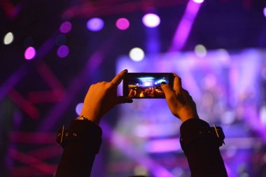Konser sırasında sahneyi cep telefonuyla kaydeden kızın elleri.