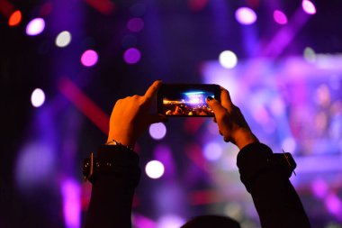 Konser sırasında sahneyi cep telefonuyla kaydeden kızın elleri.