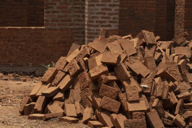A pile of burnt mud bricks, a common building material in Africa, in front of a mid construction building.