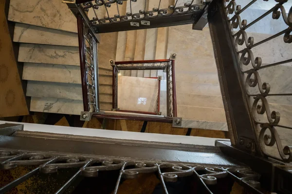 A square shaped staircase with metal railings and marble stairs, viewed from above.