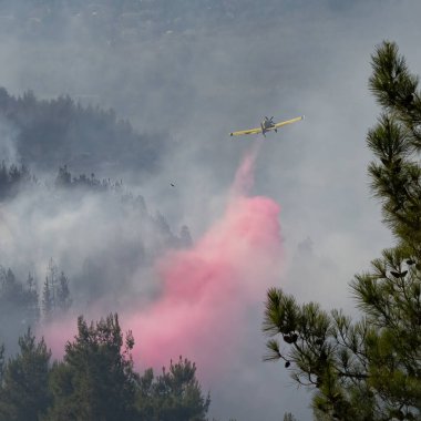 Duman içinde uçan bir itfaiye uçağı orman yangınının üzerine yangın geciktirici döker..